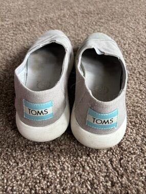 Toms women’s Slip-On Sneakers in Light Gray with Blue Logo Patch.